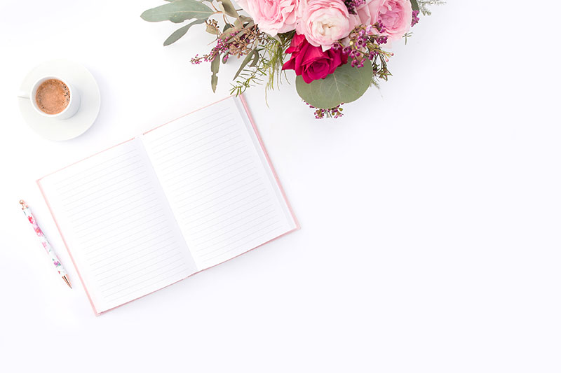 notebook, pen, flowers, and coffee on a desk